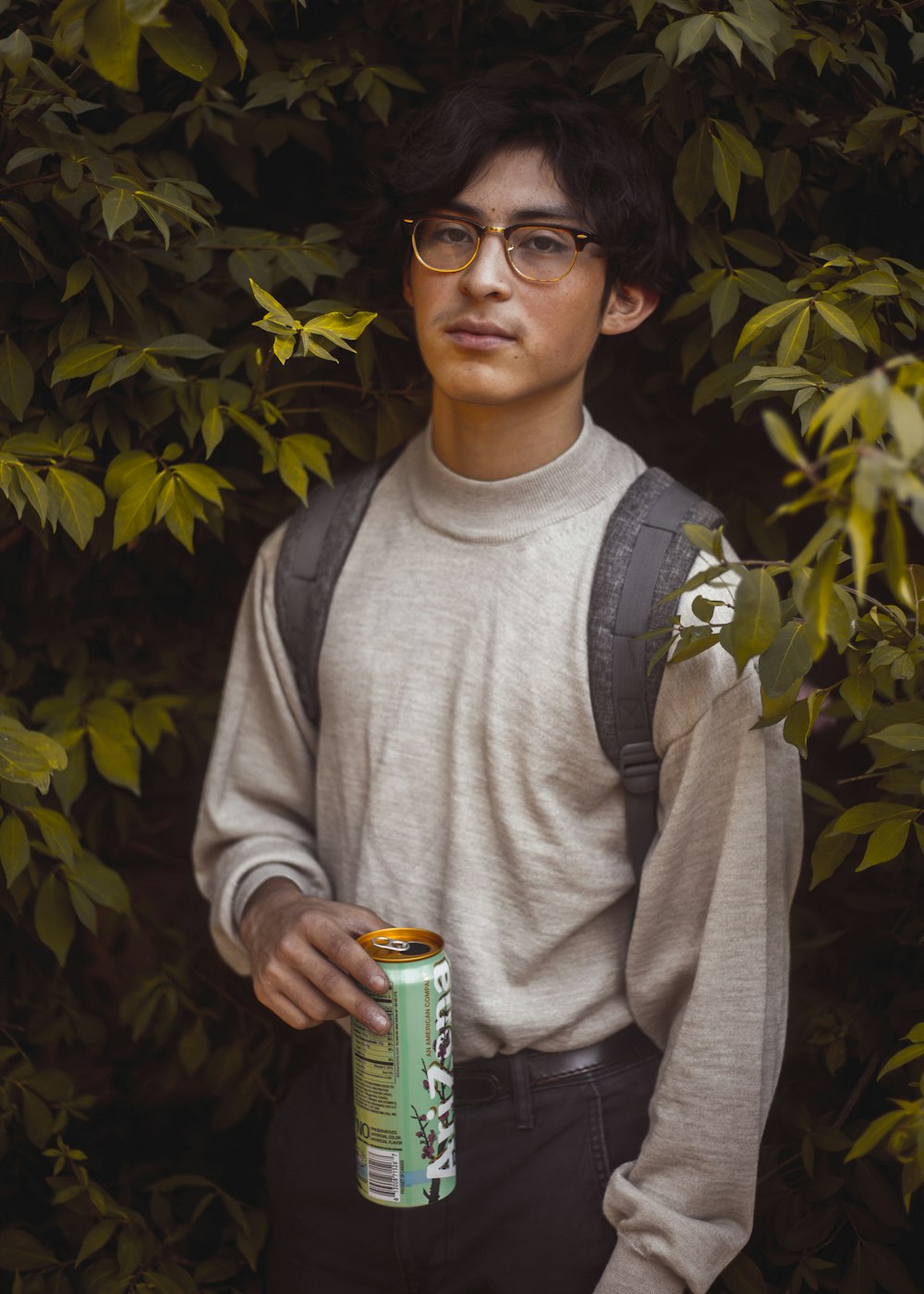 man in gray sweatshirt holding can standing near leaves