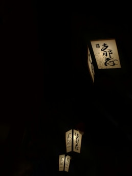 Several illuminated lanterns featuring Japanese calligraphy and an illustration of a face against a dark background, creating a contrast that highlights the warm glow of the lanterns.