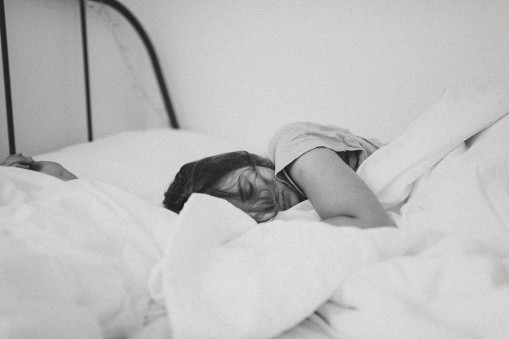 foto in scala di grigi di una donna addormentata sdraiata sul letto