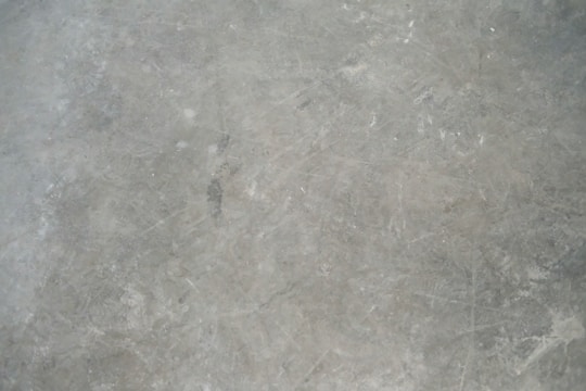 A textured grey concrete surface with visible scratches and variations in shading.