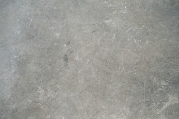 A textured grey concrete surface with visible scratches and variations in shading.