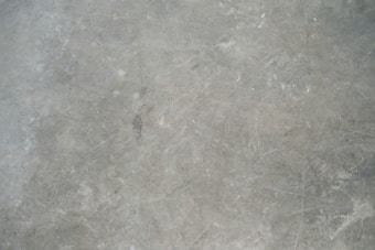 A textured grey concrete surface with visible scratches and variations in shading.