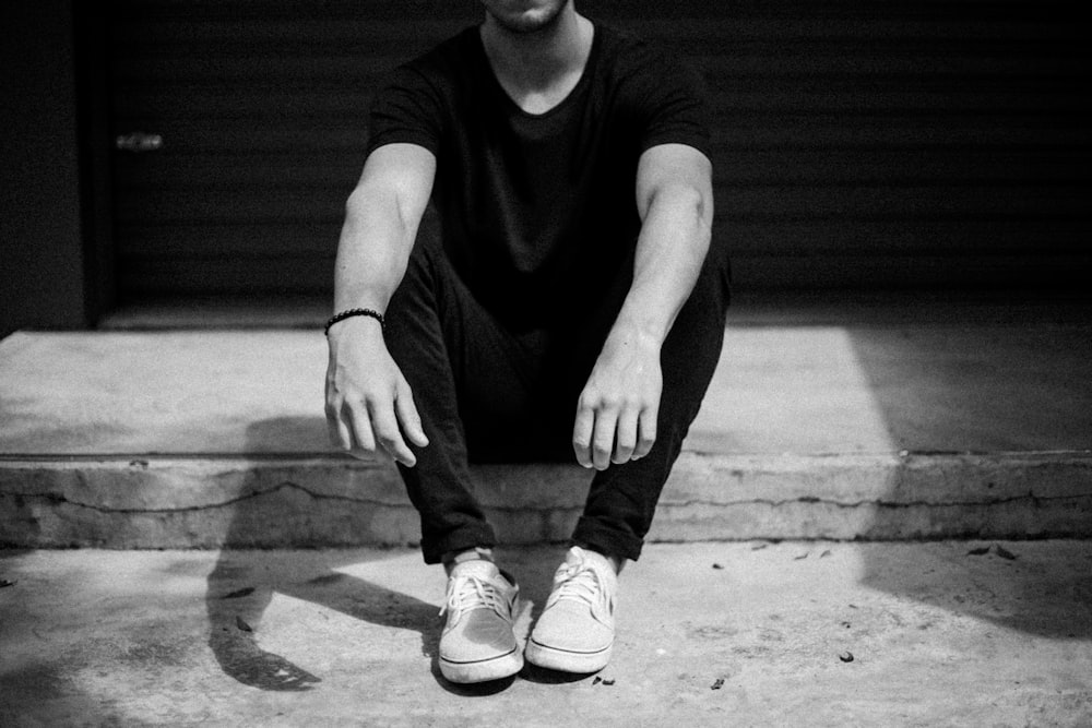 grayscale photo of man sitting on doorway