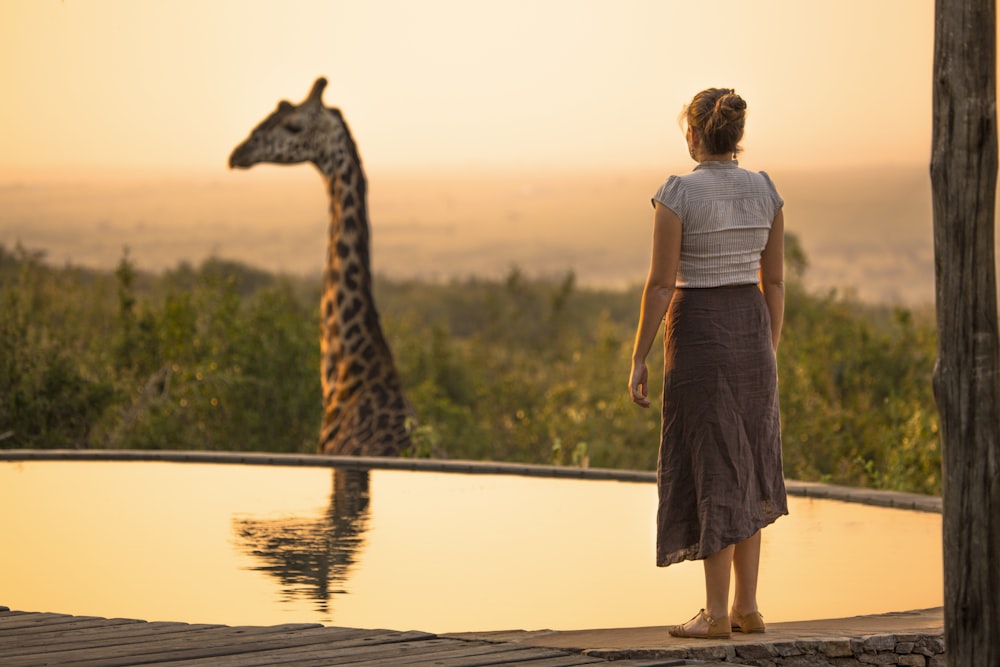woman looking at brown giraffe with reflection on water