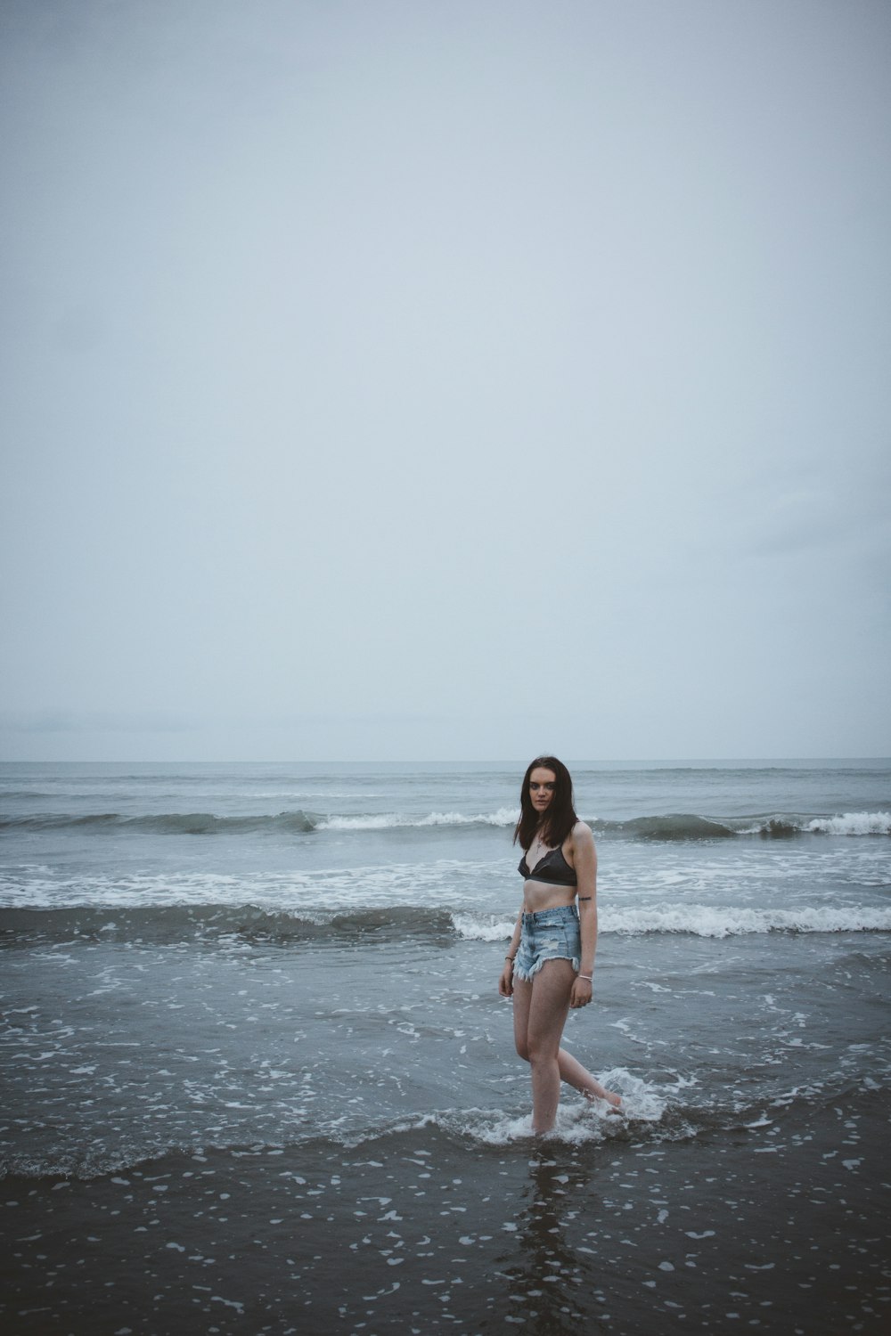 mulher que caminha na areia marrom perto do corpo de água durante o dia