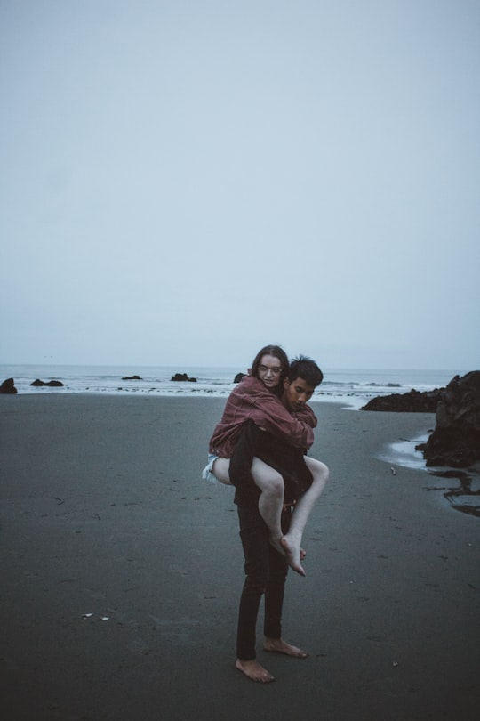 candid photography of man carrying woman at back near seashore in Sumner New Zealand