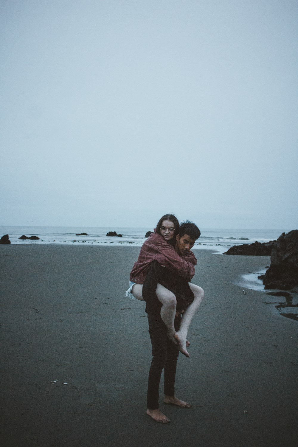 candid photography of man carrying woman at back near seashore