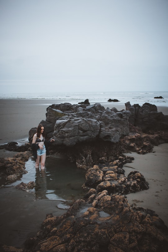 woman standing beside stone on beach shore in Sumner New Zealand