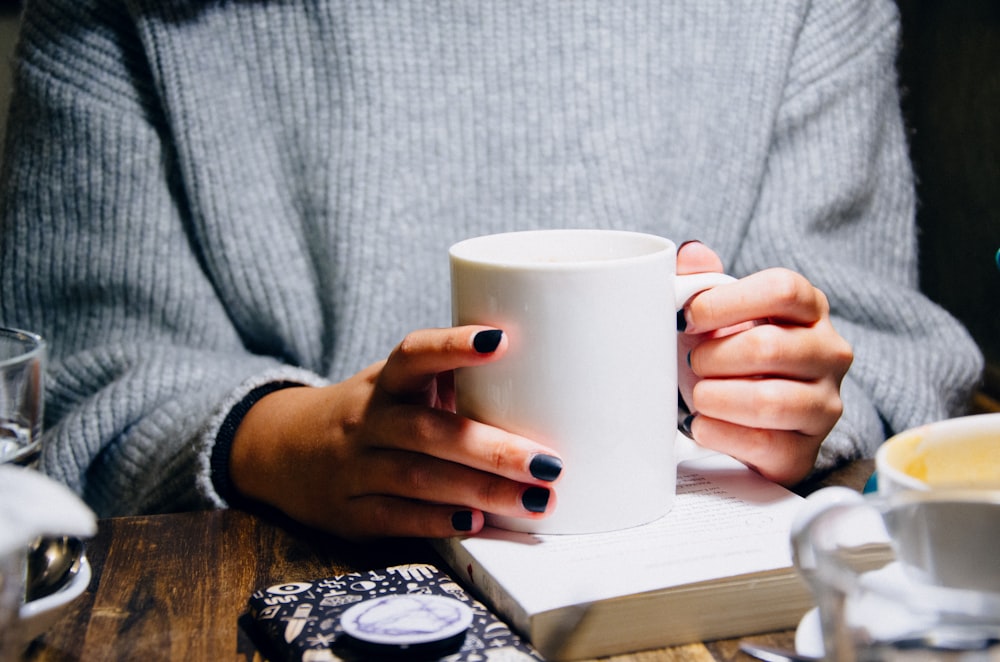 woman holding white ceramic mug near table