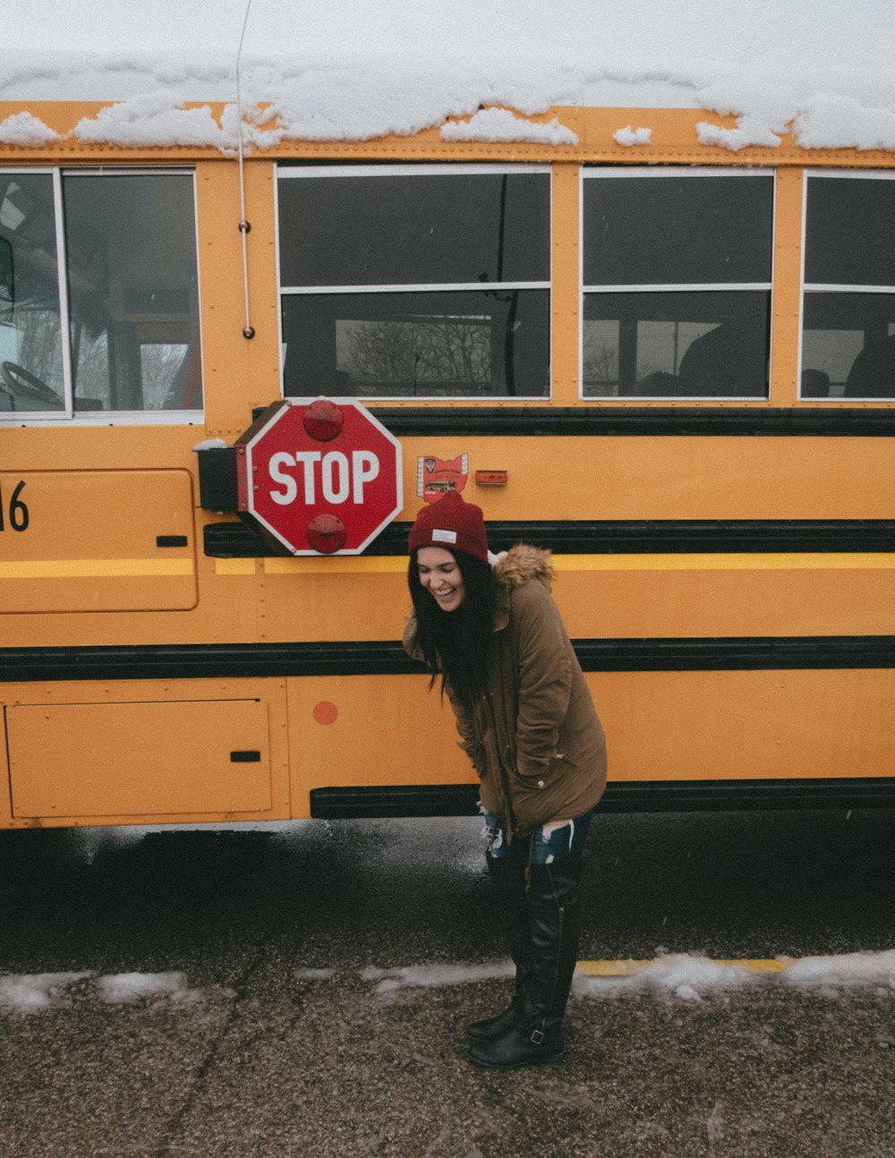 woman in brown parka coat standing in front of yellow bus