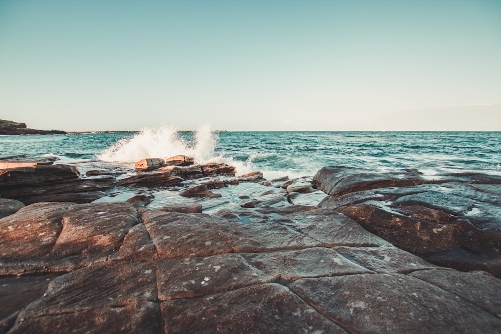 sea waves crashing on rocks under blue sky during daytime