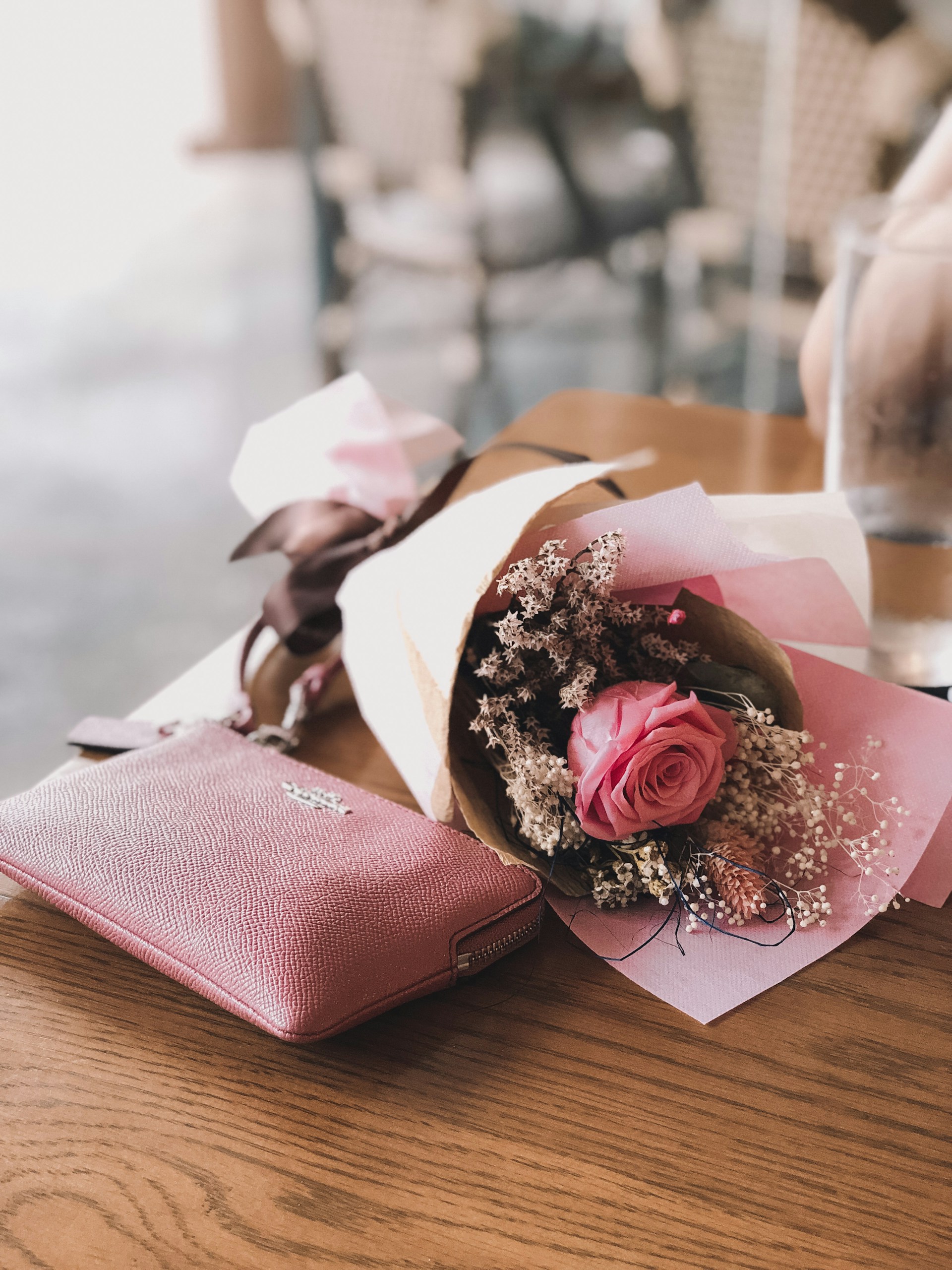 pink rose flower near the pink Coach leather wallet on brown wooden table