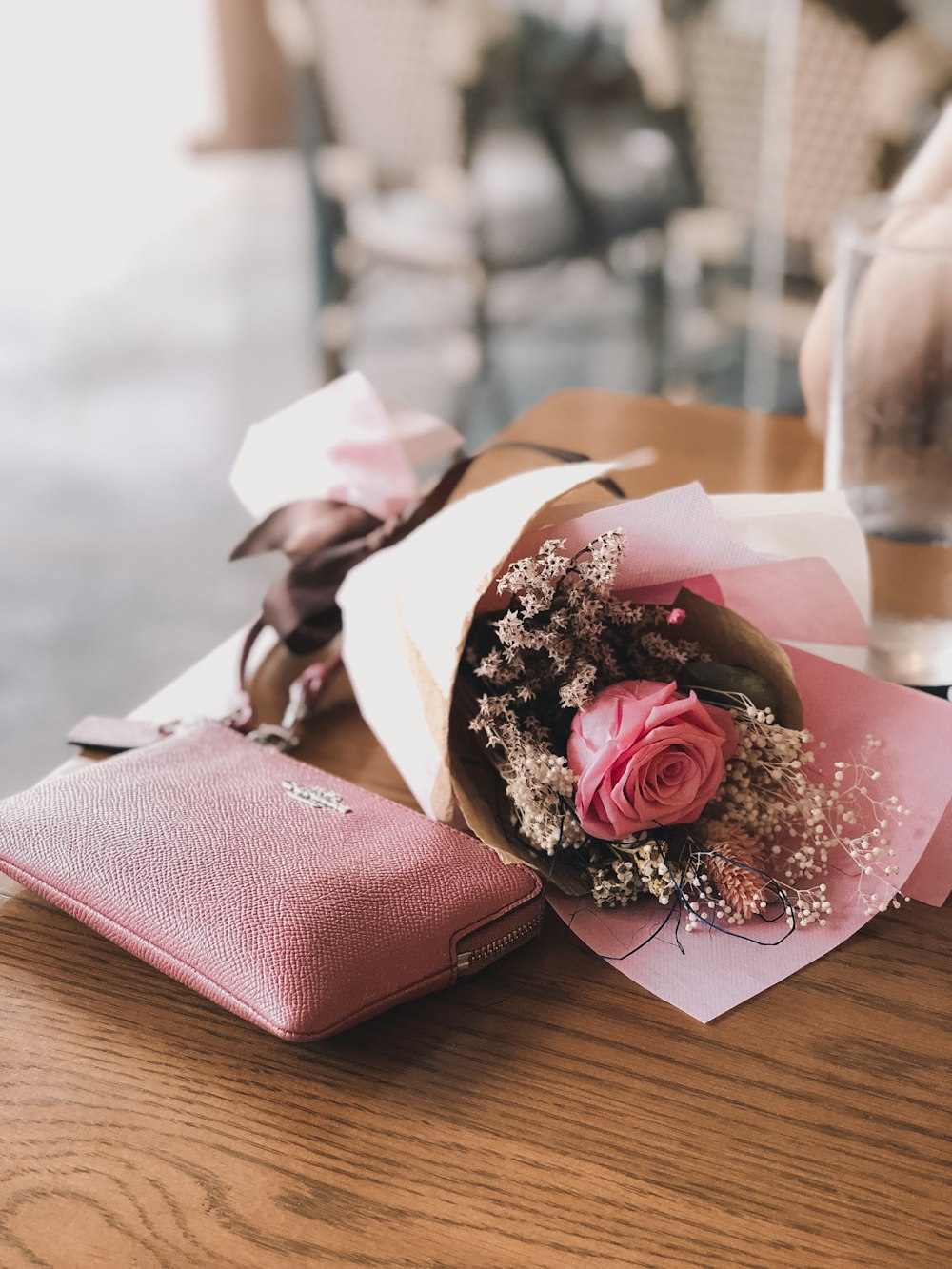 茶色の木製のテーブルにピンクのコーチの革財布の近くにピンクのバラの花