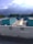 A rooftop scene with several turquoise-colored structures, possibly HVAC units, and piping. The background features lush green trees and a misty mountain range under a partly cloudy sky. The scene is well-lit with natural light that casts soft shadows.