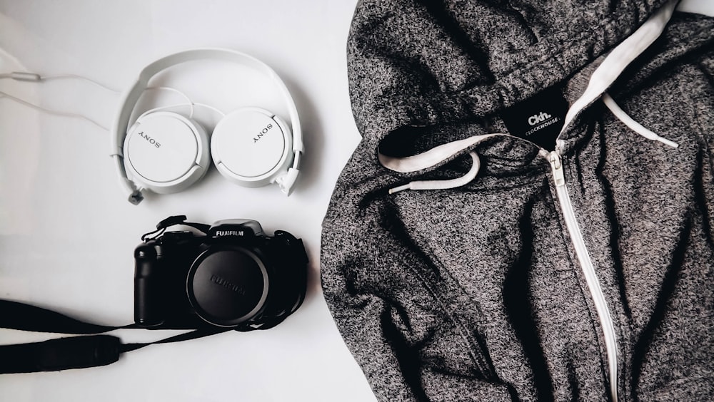 black DSLR camera and white Sony wireless headphones beside gray and white zip-up hooded jacket
