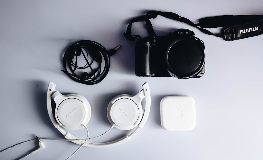 black Fujifilm DSLR camera and white corded headphones