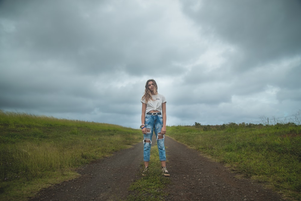 woman standing on dirt road under cloudy sky during daytime