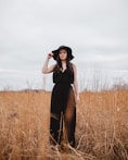 woman wearing black V-neck spaghetti-strap jumpsuit and black hat standing on brown grass field