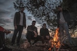 Group of smiling people sharing stories around a campfire at dusk.