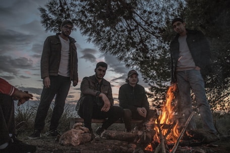 A group of campers sitting around a campfire in a forest clearing during sunset.