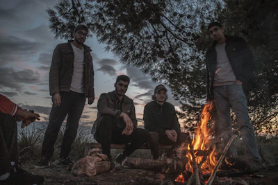 A group of men gathered around a campfire at dusk, their faces illuminated by the warm glow.