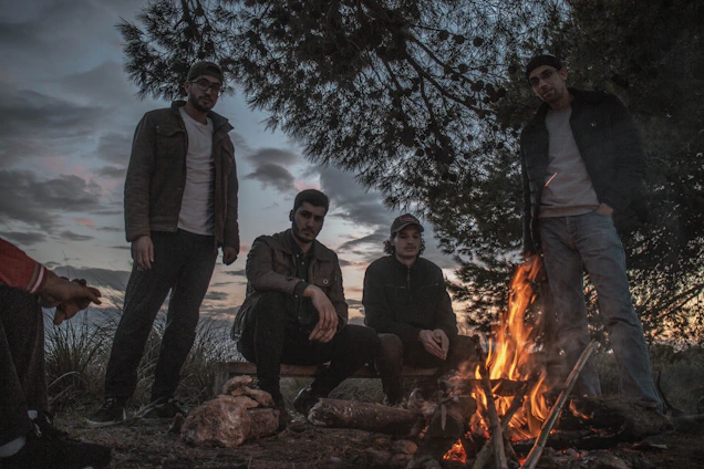 A lively group of musicians playing banjo, fiddle, and guitar around a campfire at dusk.