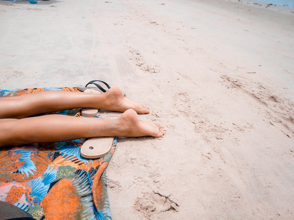 bare foot person lying on orange textile on brown sand during daytime
