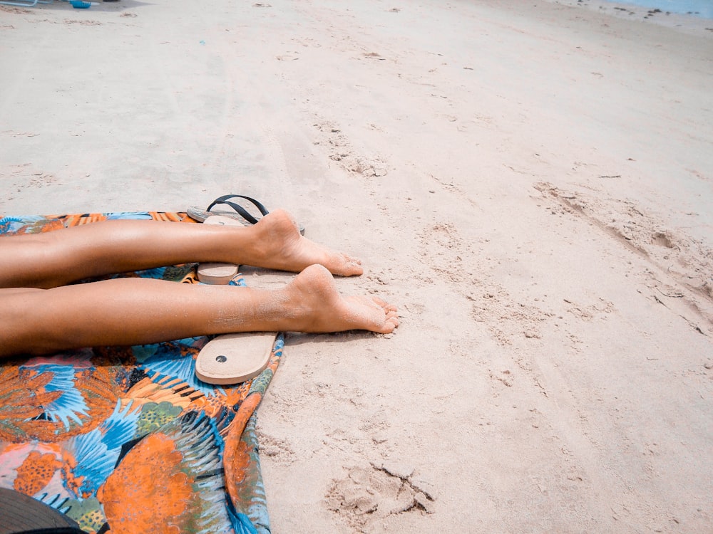 Pessoa descalça deitada em tecido laranja na areia marrom durante o dia