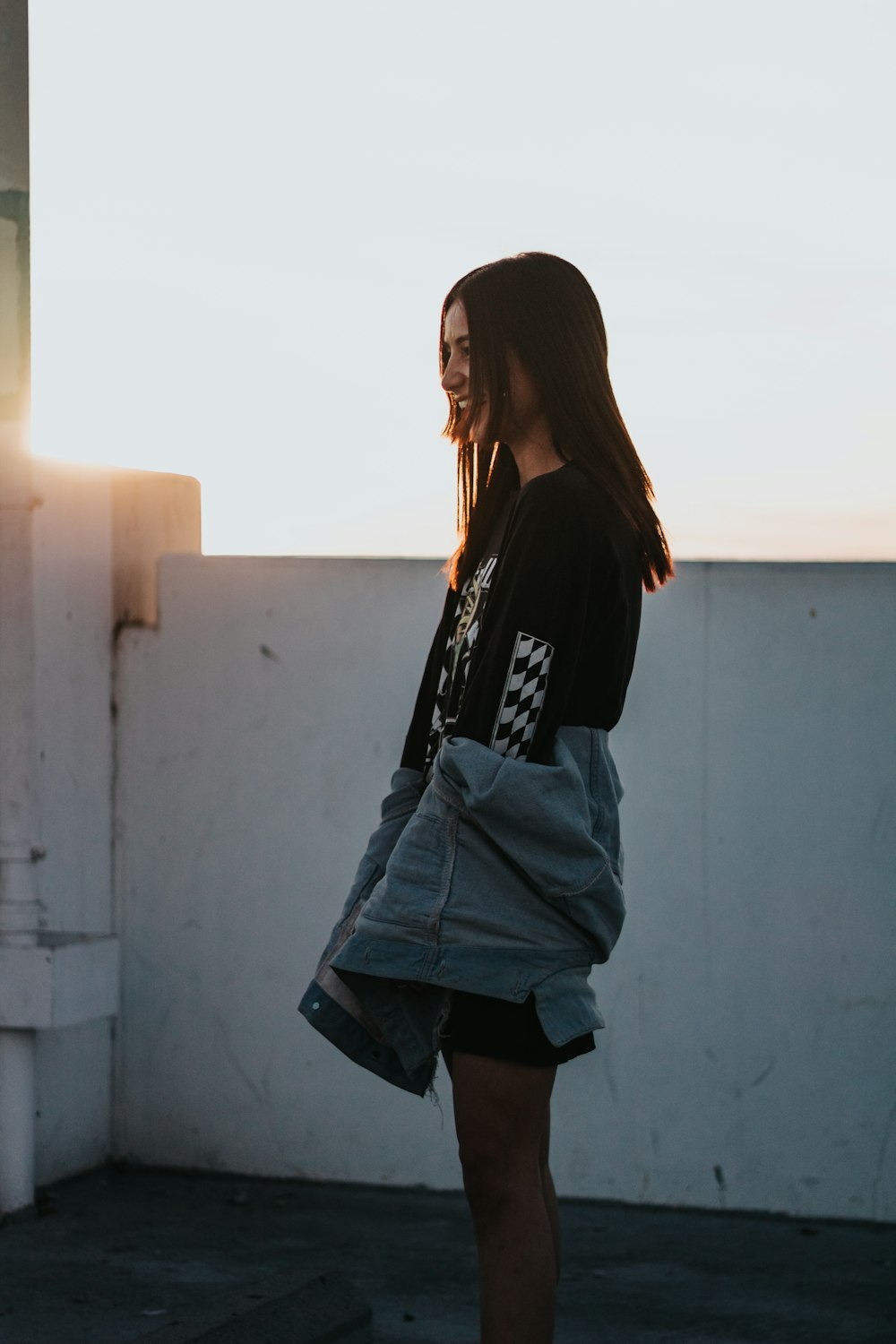 silhouette photo of girl standing beside white wall paint wearing black and white shirt and blue denim jacket