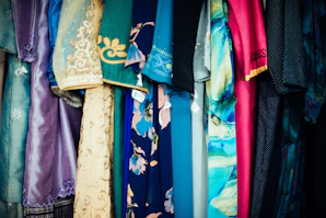 Festive kurtis arranged on a rustic wooden rack, showcasing a mix of embroidered and printed designs in royal gold and peacock green.