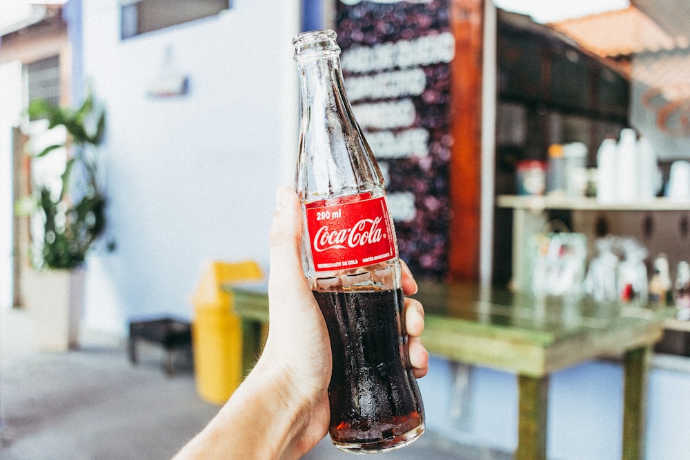 persona sosteniendo una botella de refresco de Coca-Cola