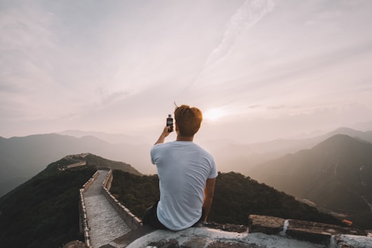 man sitting on cliff facing mountains in Great Wall of China China