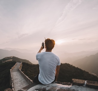 man sitting on cliff facing mountains