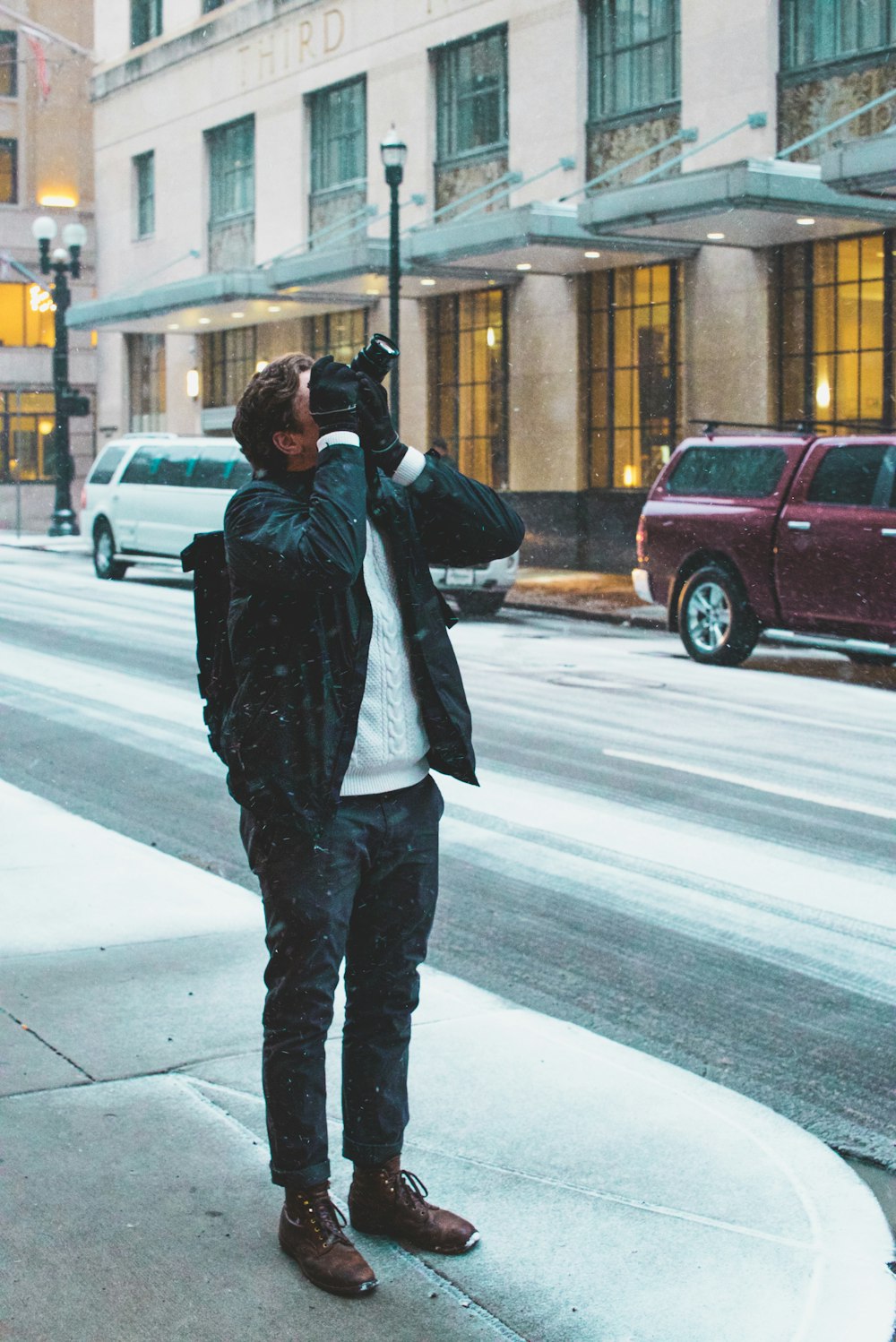 man standing on sidewalk holding DSLR camera taking picture above