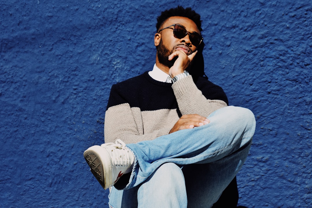 man wearing black and grey crew-neck sweatshirt leaning on blue concrete wall