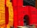 Large, vibrant letters adorned with intricate tribal-style illustrations. The design features small human figures engaged in various activities, constructed in a traditional, artistic pattern. The letters are primarily in shades of red and yellow, with black line drawings that depict scenes and motifs inspired by indigenous art.