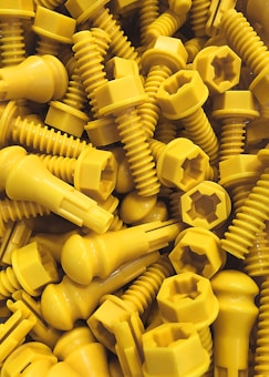 A collection of bright yellow plastic screws and bolts with a mix of hexagonal and rounded heads scattered randomly.
