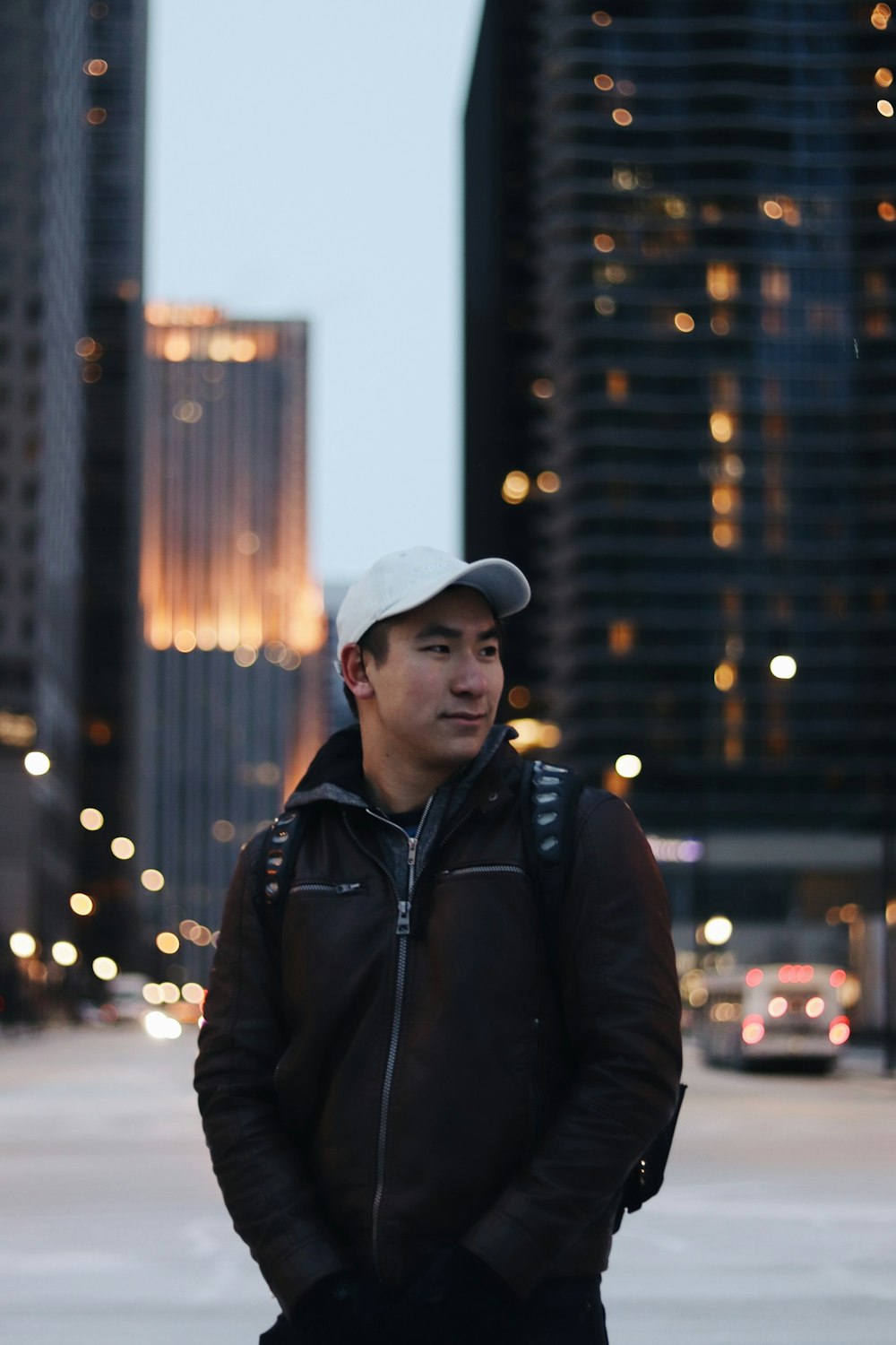 man wearing black zip-up jacket standing near high-rise building