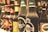 A row of various beer bottles with distinct labels, including brands such as Carlsberg and Tuborg. The bottles are arranged side by side on a shelf with a slightly blurred background, indicating a bar or store setting.