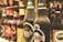 A row of various beer bottles with distinct labels, including brands such as Carlsberg and Tuborg. The bottles are arranged side by side on a shelf with a slightly blurred background, indicating a bar or store setting.
