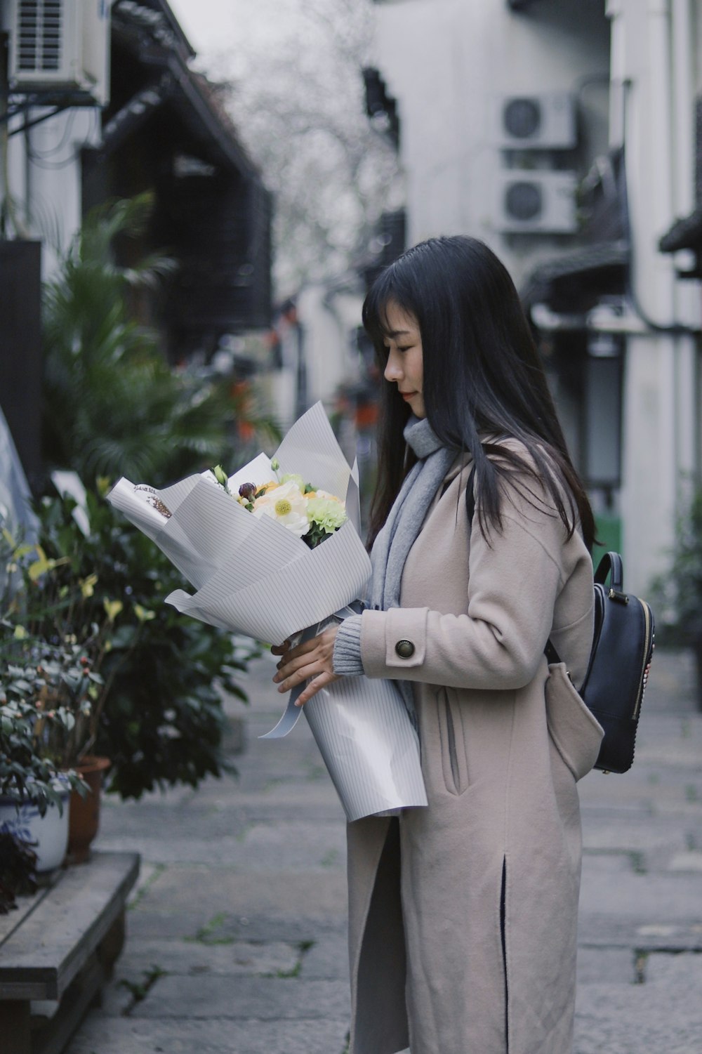 緑の葉の植物のそばに立つ花束を持つ女性