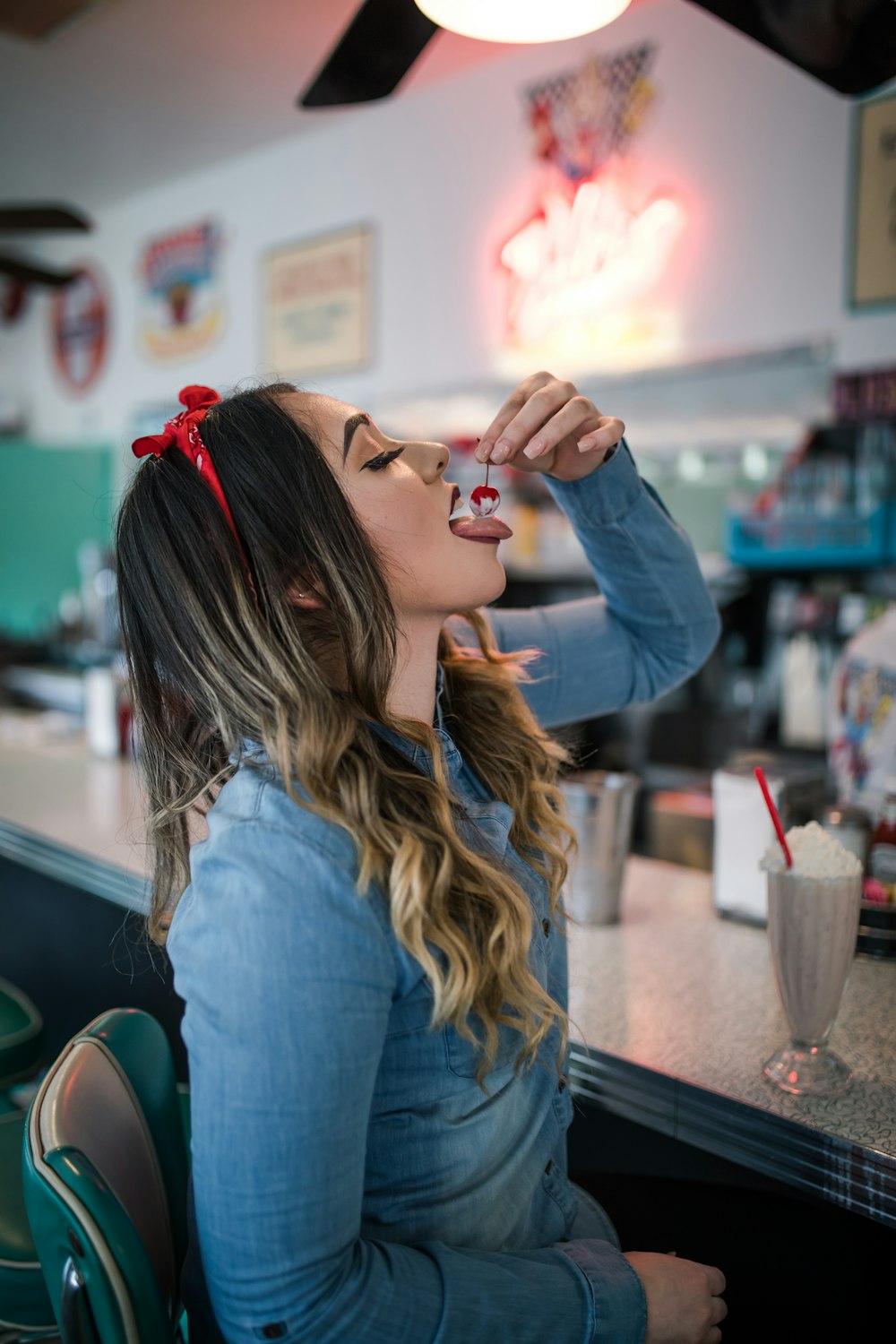 woman wearing blue long-sleeved shirt eating cherry from parfait inside room