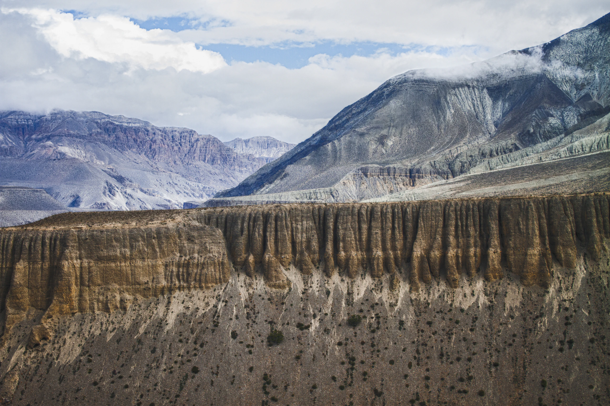 Wide view of Mustang's ochre wind-carved cliffs and high-desert badlands beneath snow-streaked ridges, Nepal
