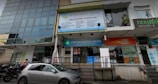The image depicts a street view of a building with various businesses. A large sign for Ashford Dental Centre is prominently displayed above the entrance. Several other signs are visible, including one for a place named 'nourish naturally.' There is a parked car and a few motorcycles in front of the building, and a couple of pedestrians are nearby.