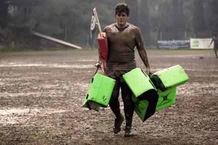 man covered in mud carrying leather training pads
