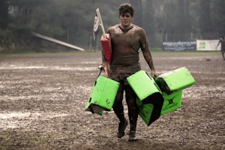 man covered in mud carrying leather training pads