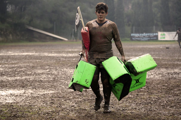man covered in mud carrying leather training pads
