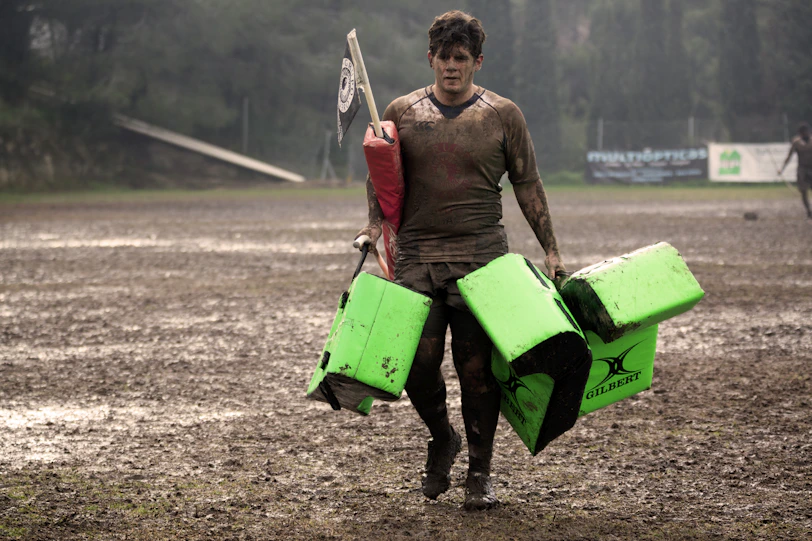 man covered in mud carrying leather training pads
