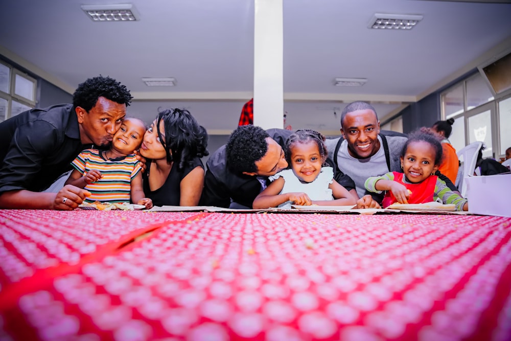 mulher e três homens com três crianças na frente da mesa com pano vermelho