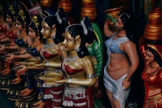 A colorful display of intricately detailed figurines, each dressed in elaborate traditional attire. The figures hold various objects, with vibrant colors and ornate decorations covering their surfaces. They stand in close proximity, suggesting a sense of unity and cultural significance.